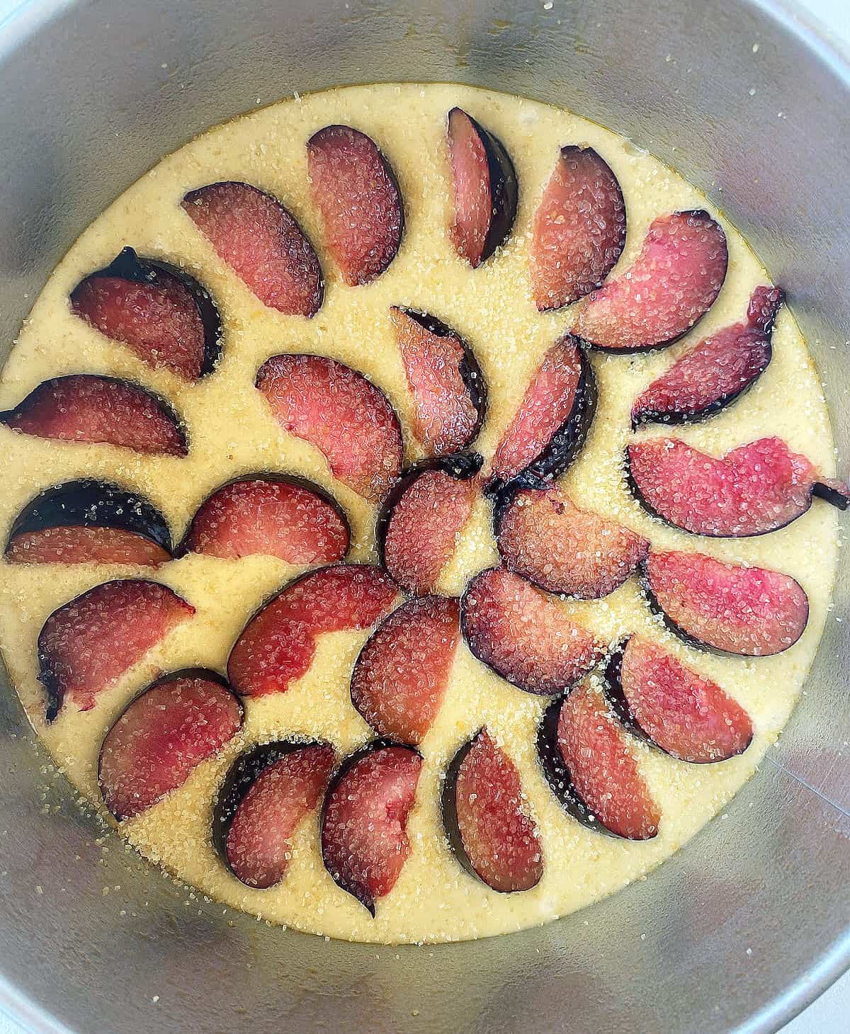 Top view of plum wedges on top of cake batter. Metal round pan.