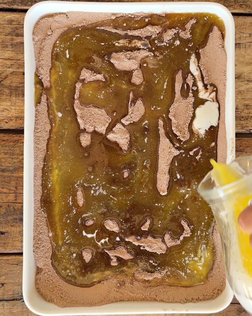 Melted butter drizzled over chocolate cake mix in a rectangular white dish. Wooden surface.