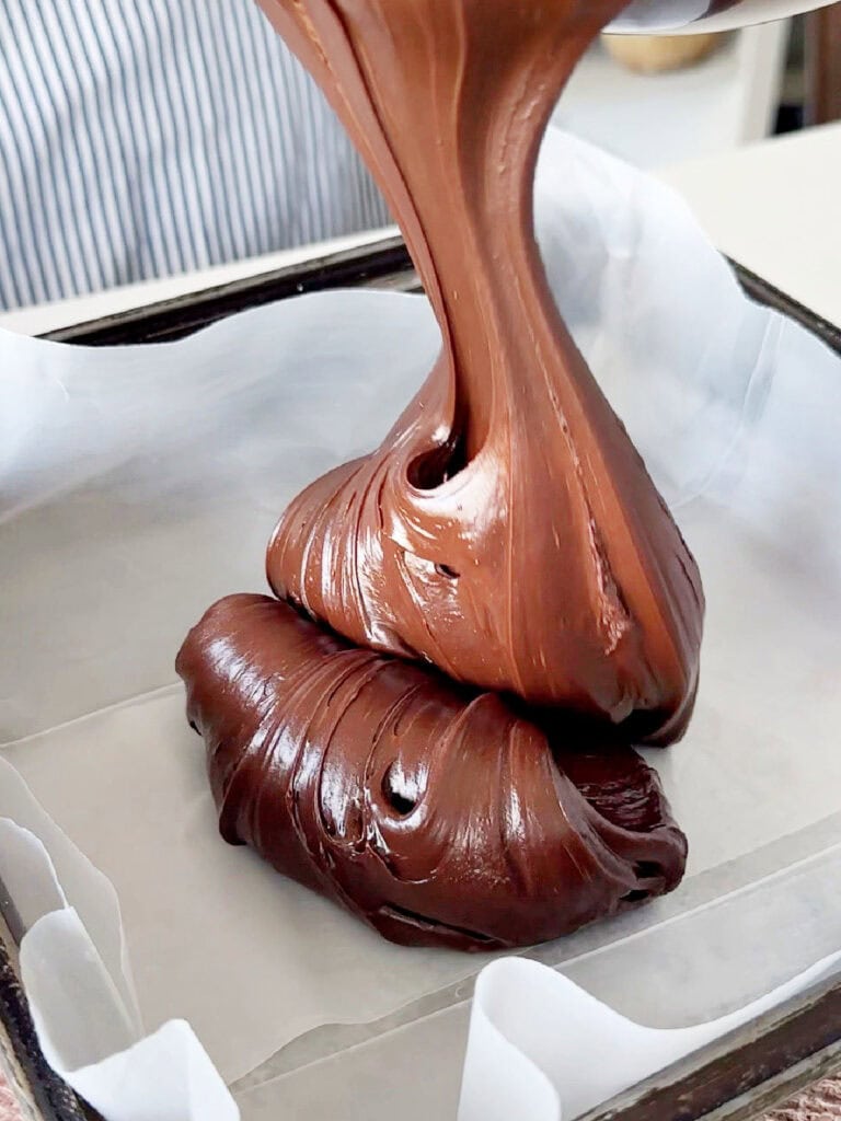 Pouring chocolate fudge mixture onto a lined pan.