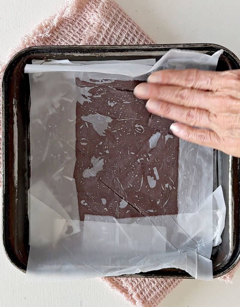 Patting freezer sheets to adhere on fudge mixture in a metal pan. 
