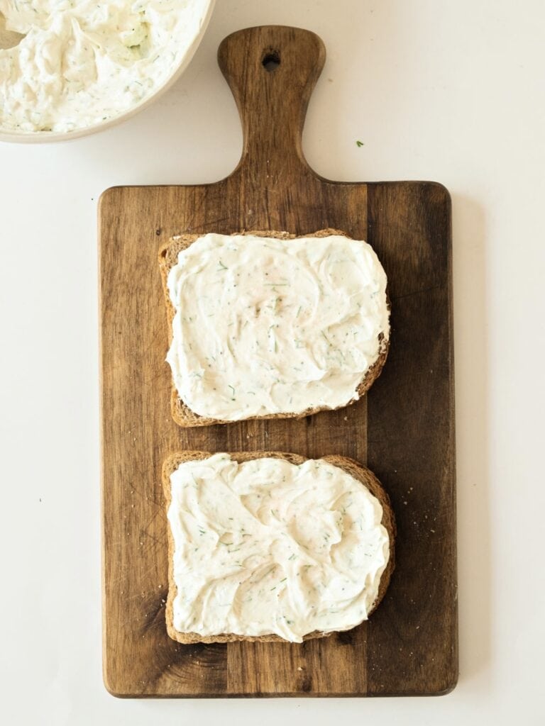 Cream cheese spread on two whole wheat bread slices on a wooden board. White background.