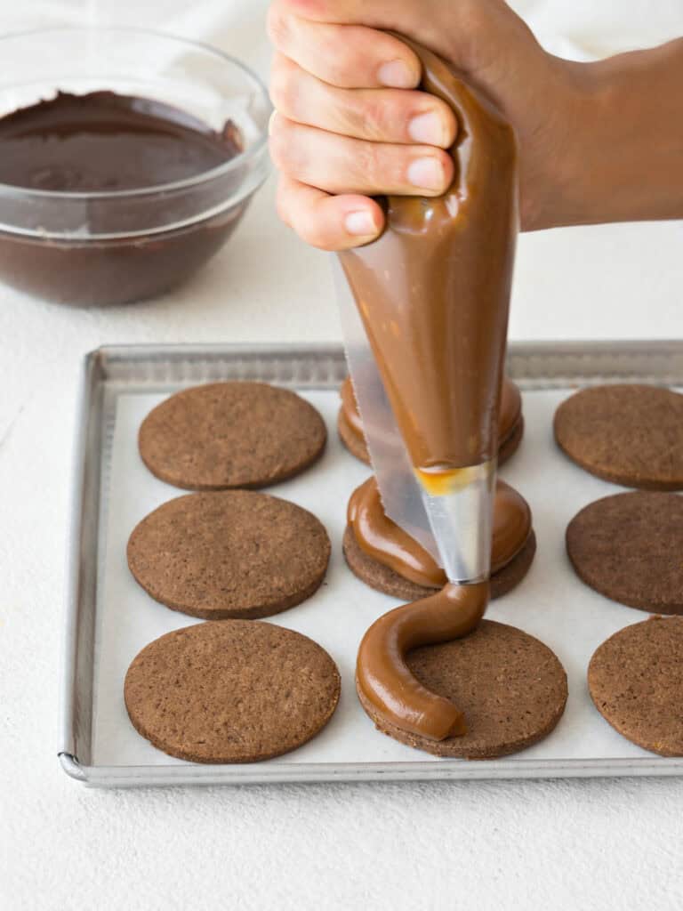 Piping dulce de leche onto chocolate cookie rounds. Metal baking sheet.