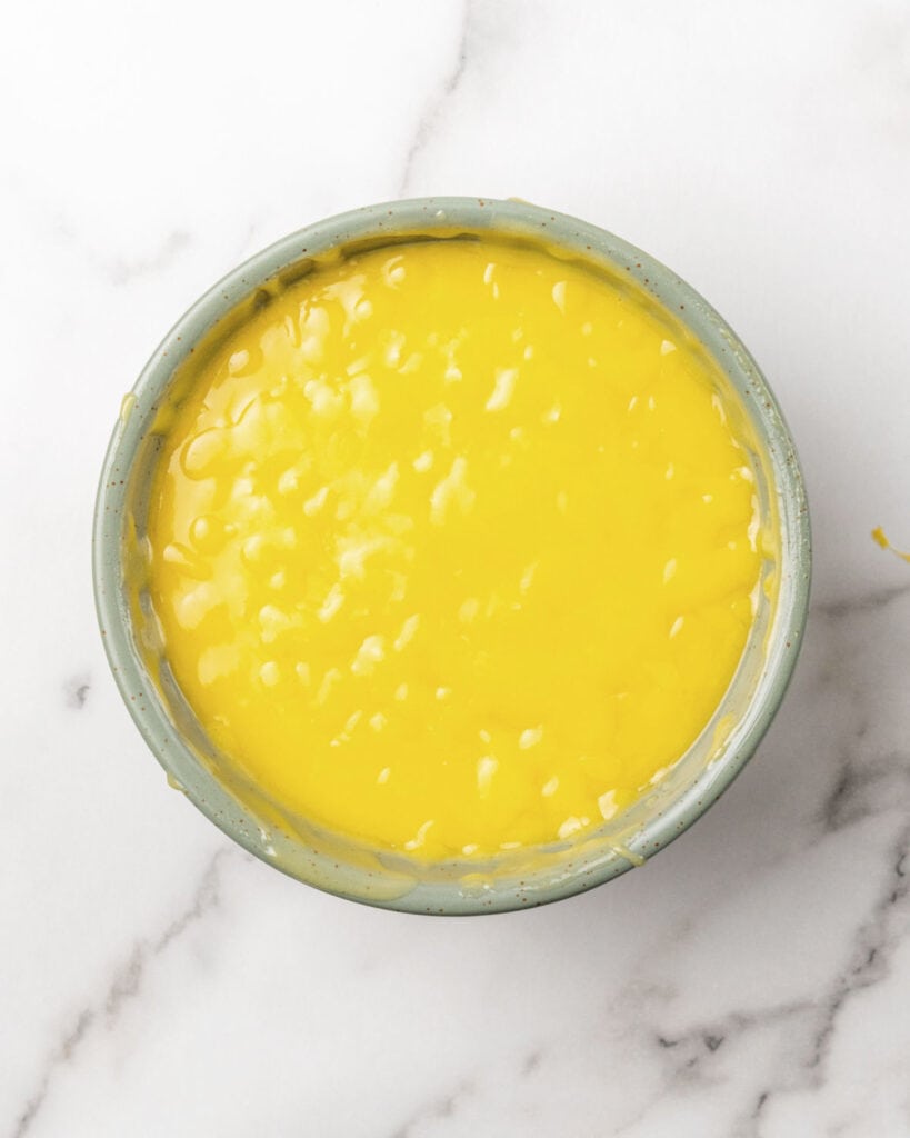 Gray bowl of passion fruit curd on a white marble surface.