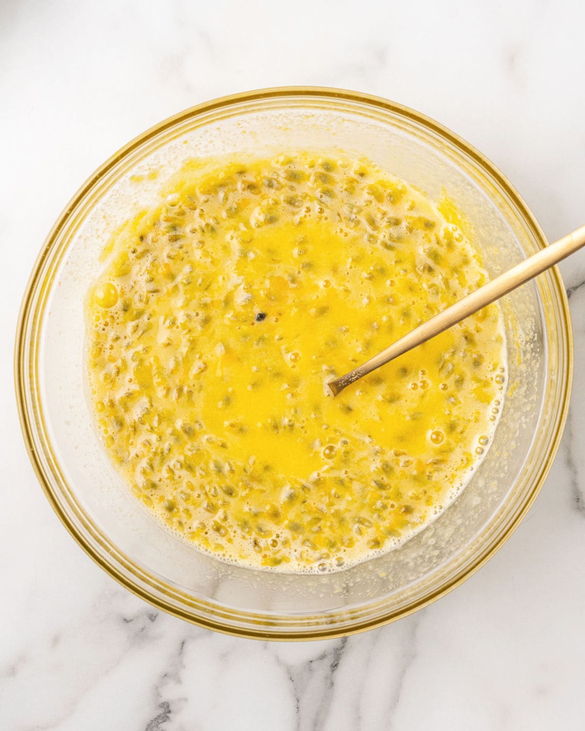 Seeded passion fruit pulp and yolks in a glass bowl. Wooden spoon. White background.