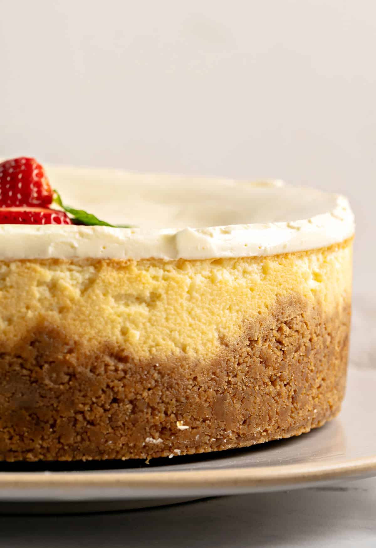 Side view of cheesecake with crumb crust and sour cream topping. Fresh strawberries.