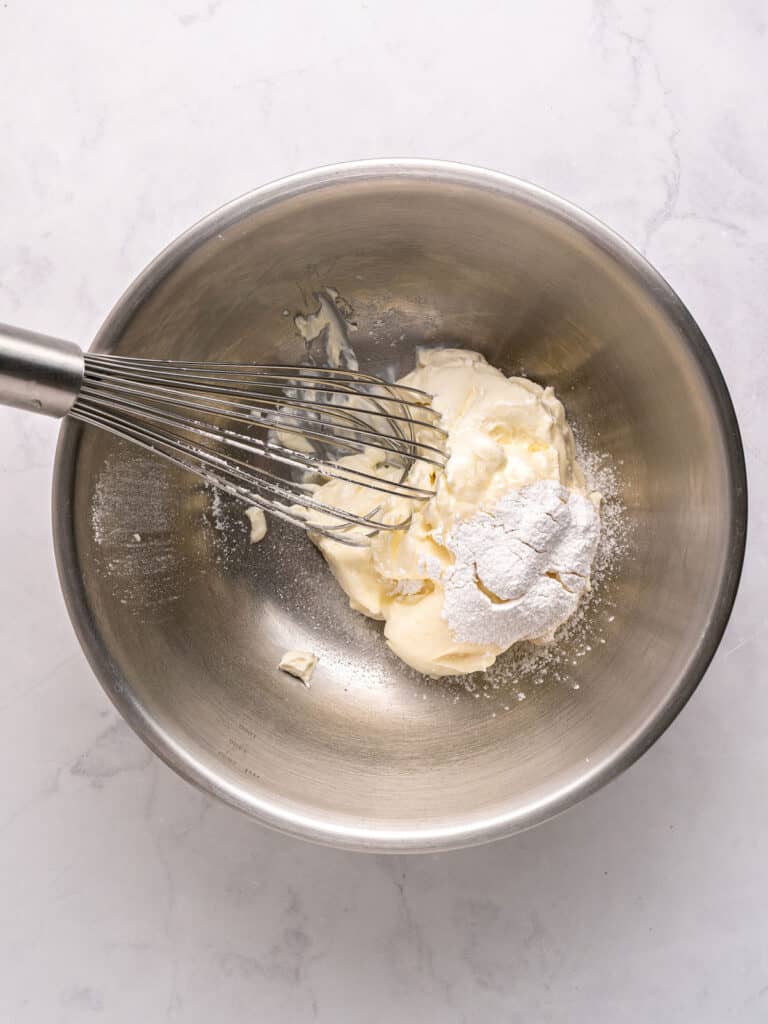 Metal bowl with sour cream and powdered sugar. Metal whisk.