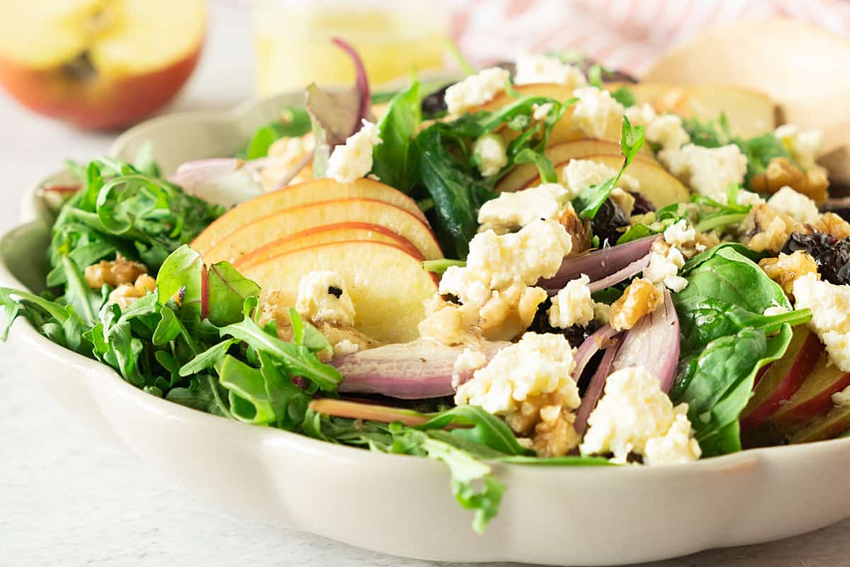 Close up of shallow white bowl with apple green salad with walnuts and feta.