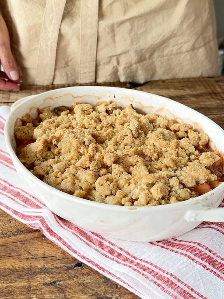 Striped red cloth with white dish of rhubarb crumble. Beige background.