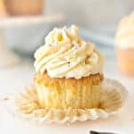 Close up frosted vanilla cupcake with sprinkles. Flat paper liner. White gray background.