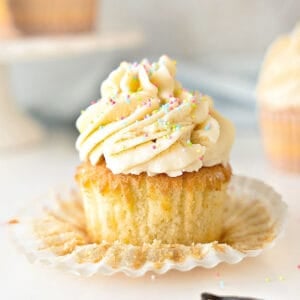 Close up frosted vanilla cupcake with sprinkles. Flat paper liner. White gray background.