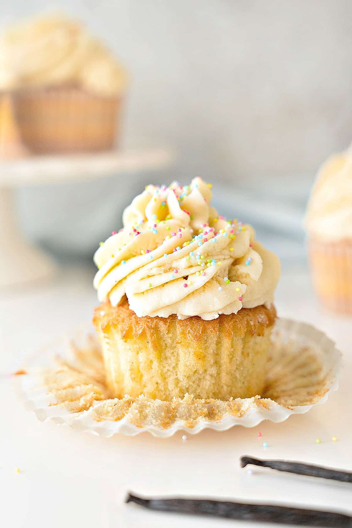 Single frosted vanilla cupcake on an opened paper liner. Light gray background.