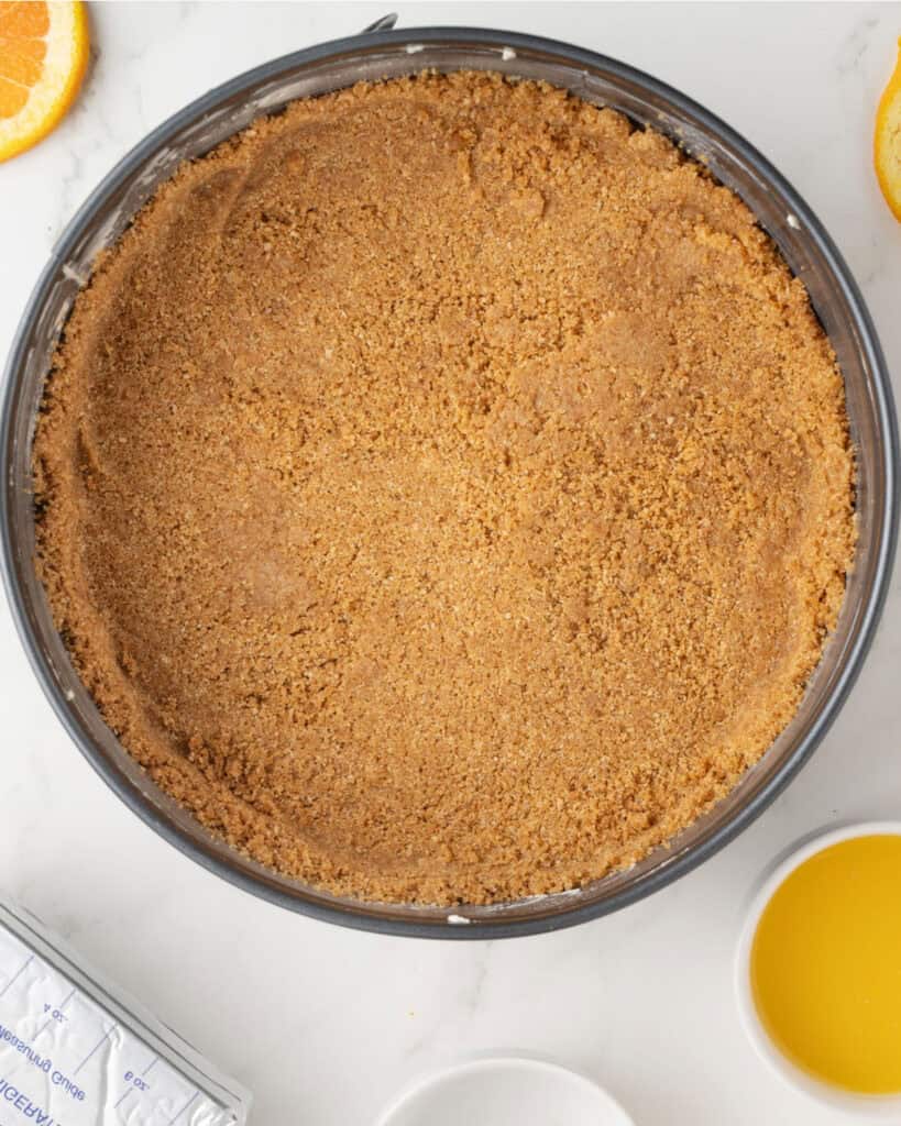 Graham cracker crust in a dark metal cake pan.
