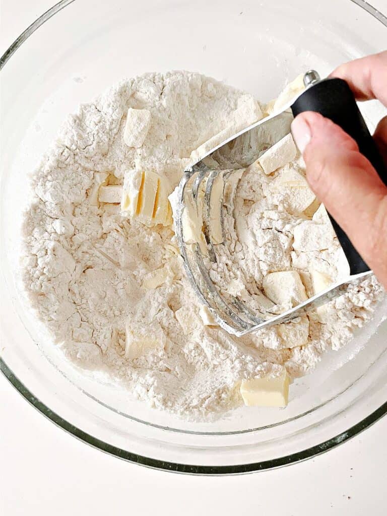 Cutting in butter into flour mixture in a glass bowl with a pastry cutter.