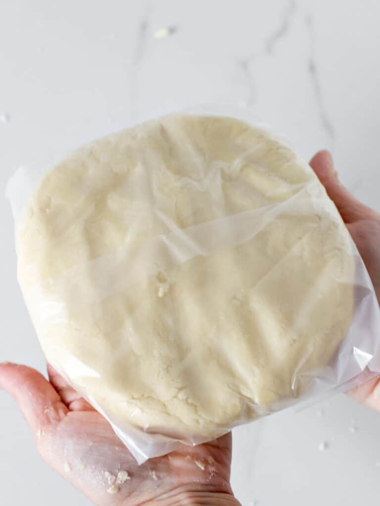 Wrapped disc of pie crust on a white marble surface.