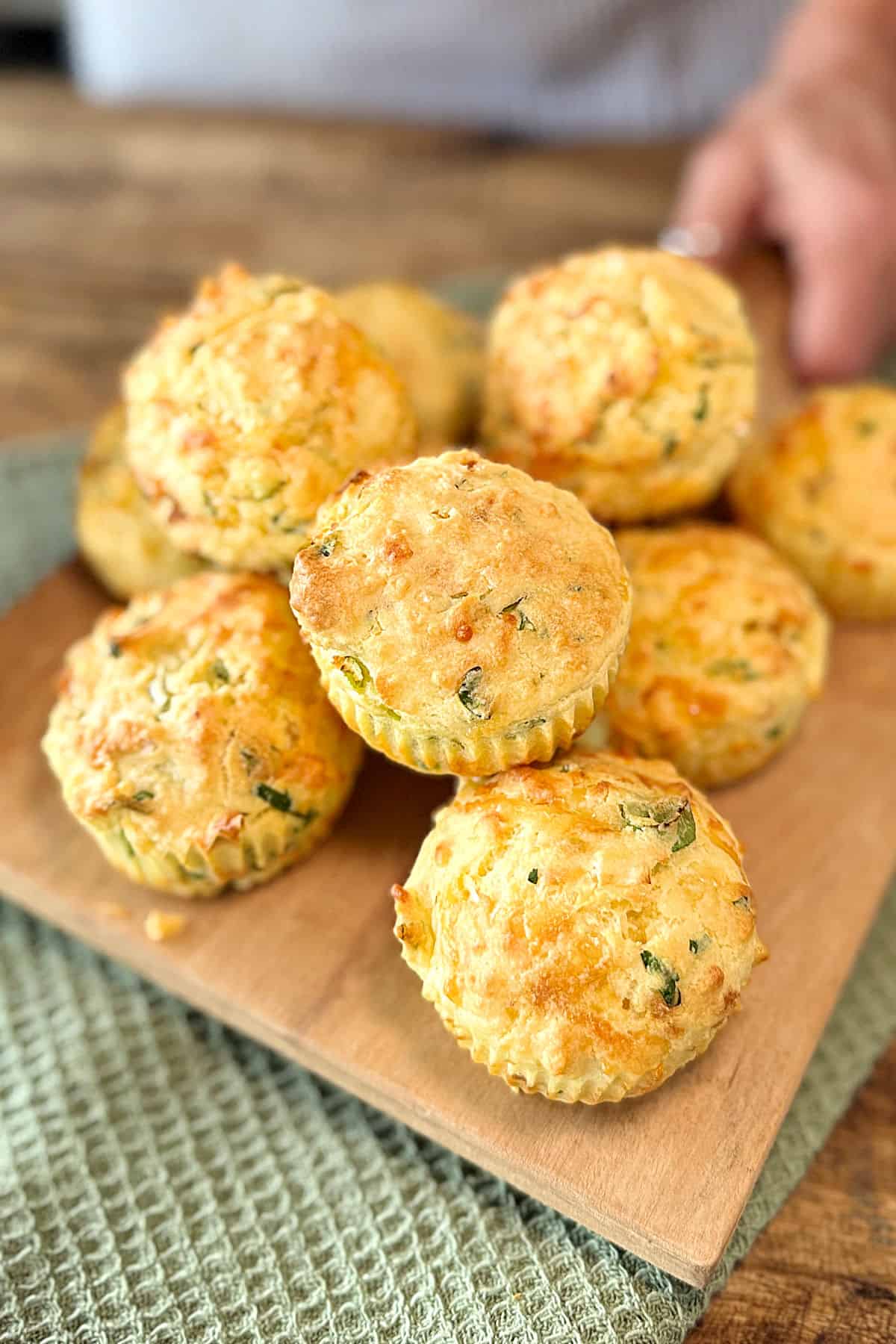 Pile of savory muffins on a wooden board and table. Green towel.