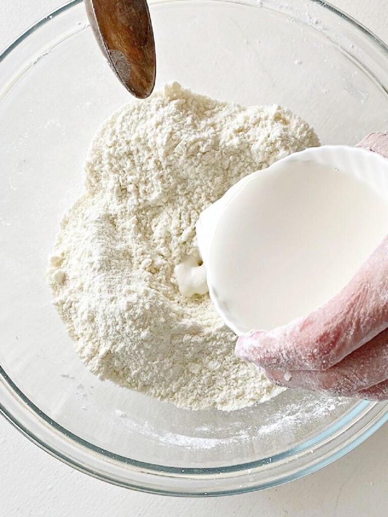 Pouring milk into flour mixture in a glass bowl. White background.