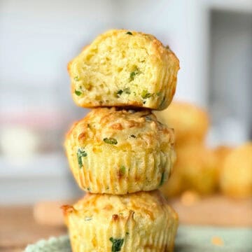 Cheese savory muffins stacked. Top one is bitten. Gray blurred background.