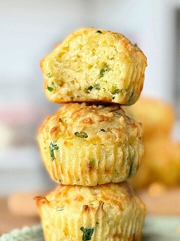 Cheese savory muffins stacked. Top one is bitten. Gray blurred background.