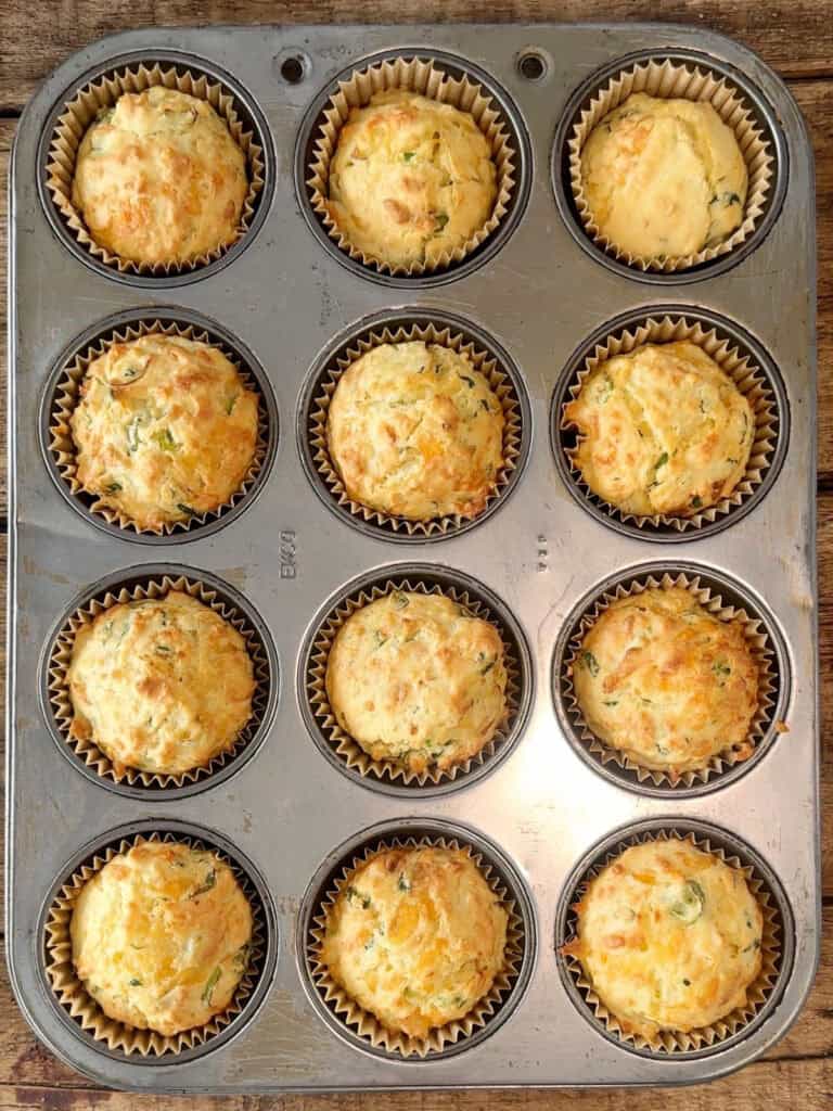 Top view of baked cheese green onion muffins on the metal pan.