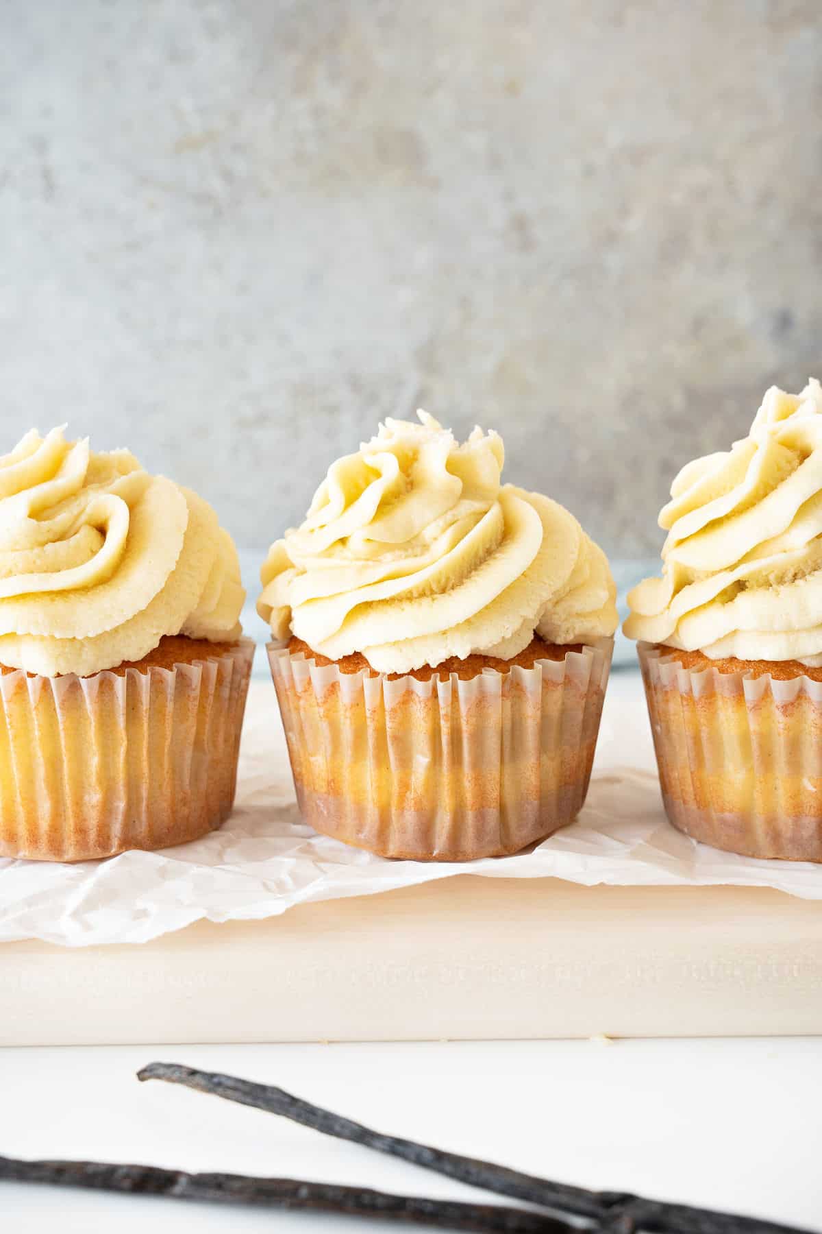 Frosted vanilla cupcakes in a row. White surface, gray background.