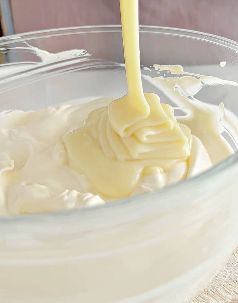 Condensed milk poured over whipped cream cheese in a glass bowl.