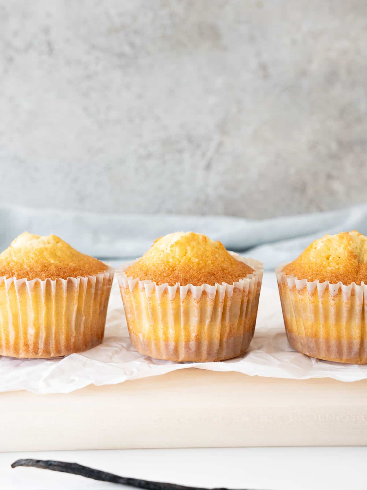 Three vanilla cupcakes in paper liners. White and gray background.