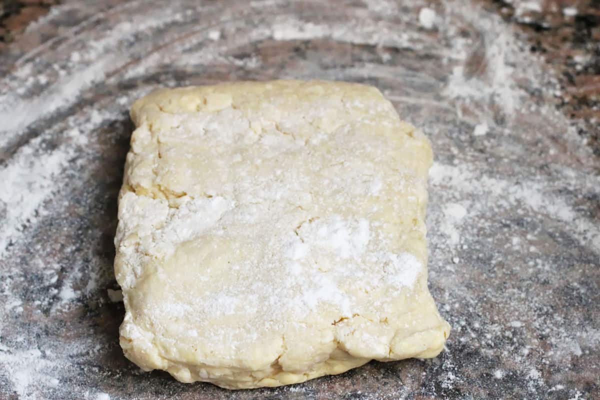 Square of rough danish dough on floured brown marble.