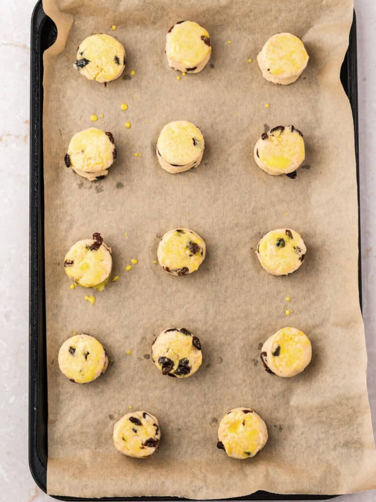 Unbaked raisin scones on beige parchment paper.