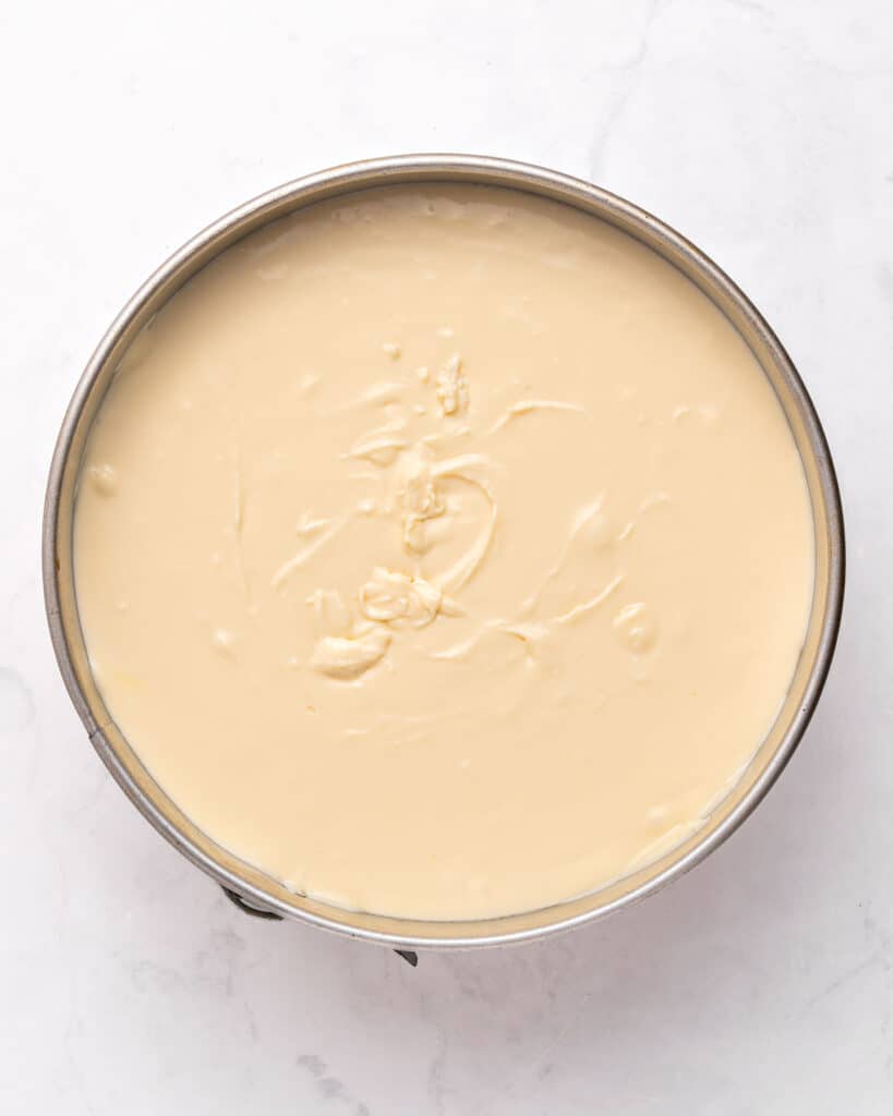 Cheesecake filling in a round springform cake pan. White background.