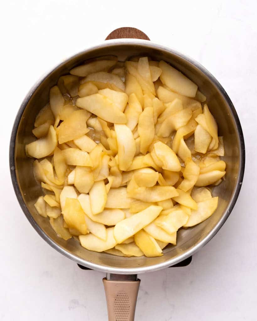 Large metal skillet with cooked apple slices. White background.