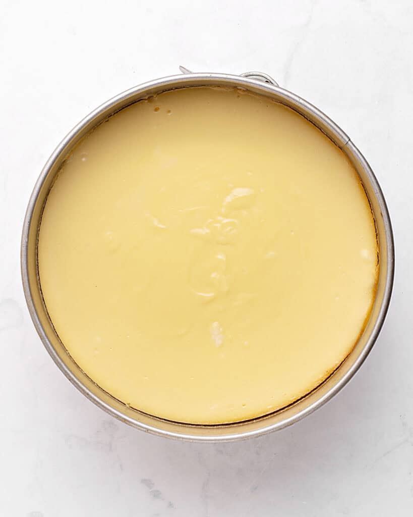 Baked cheesecake in a round metal springform pan. Top view.