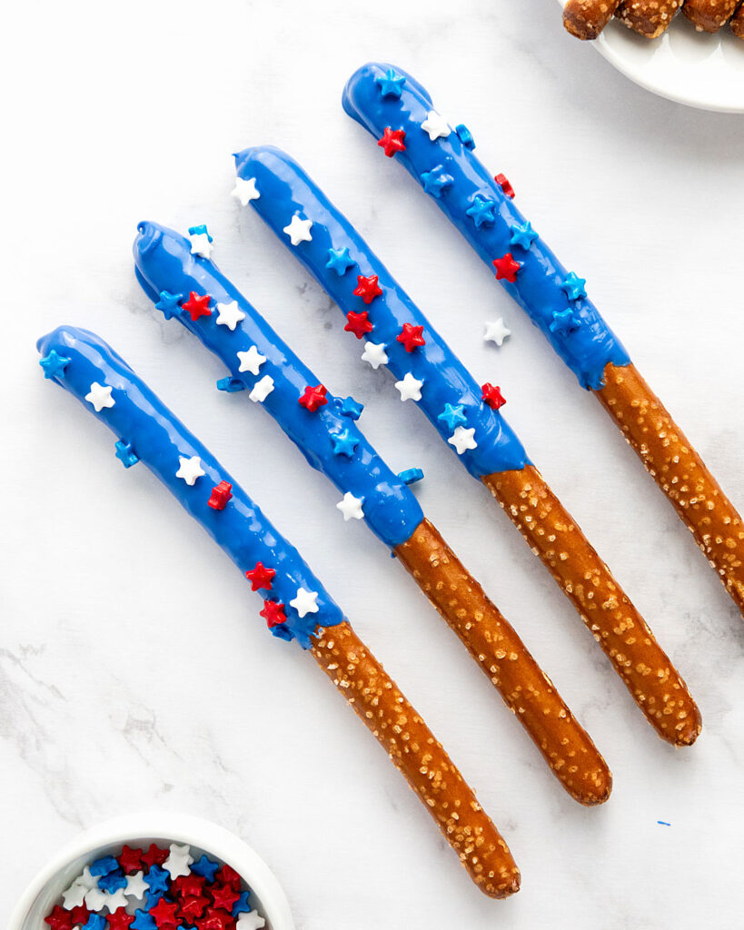 Four blue chocolate-covered pretzel rods with sprinkles. White background.