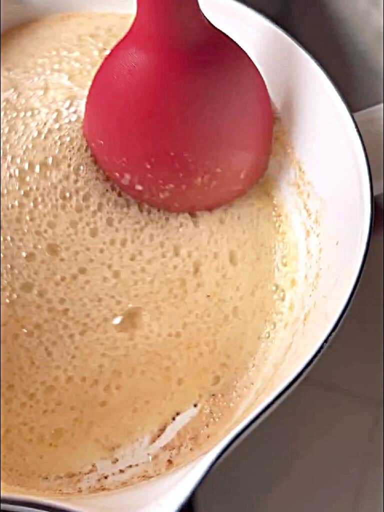 White saucepan and red spatula with foaming browned butter.