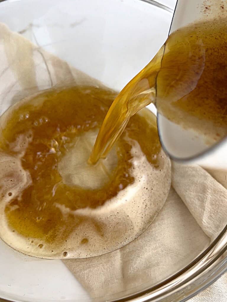 Pouring brown butter into a glass bowl from a white saucepan. Beige linen underneath.