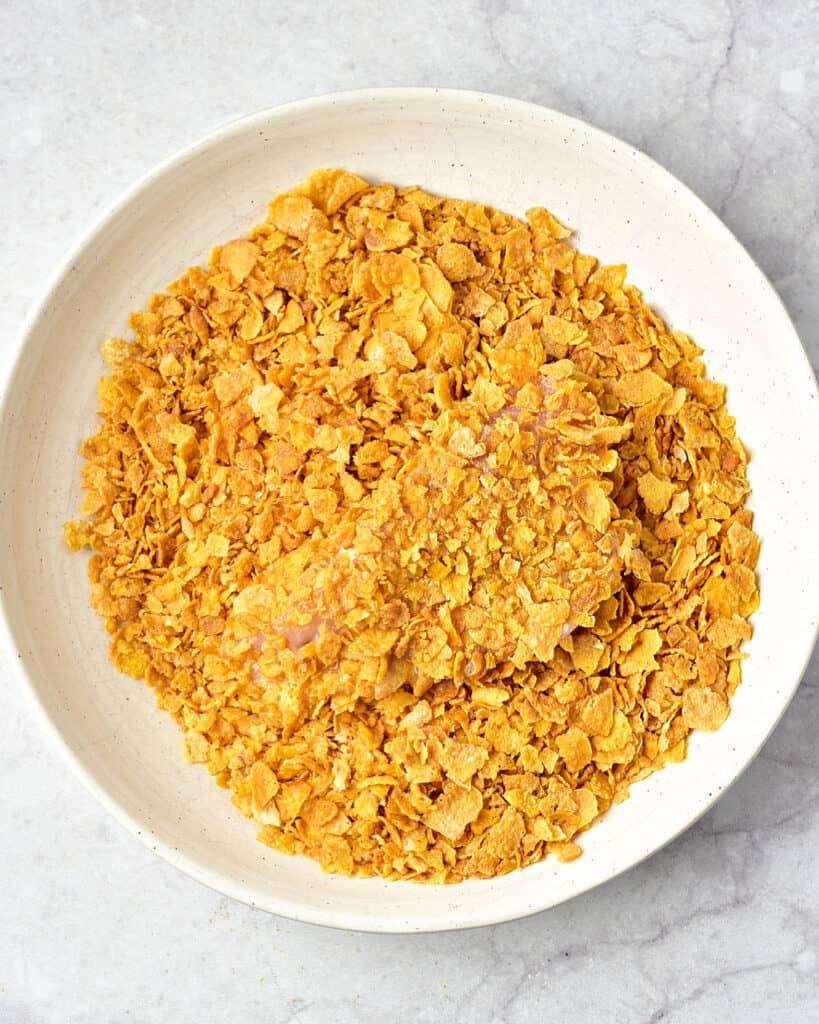Light gray surface with white bowl of cornflake and piece of chicken breast.