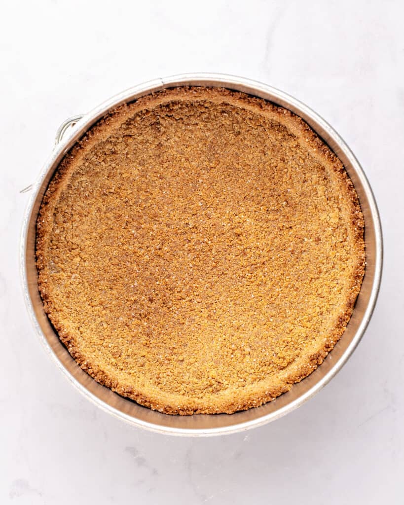 Graham cracker crust in a round metal cake pan. White background.