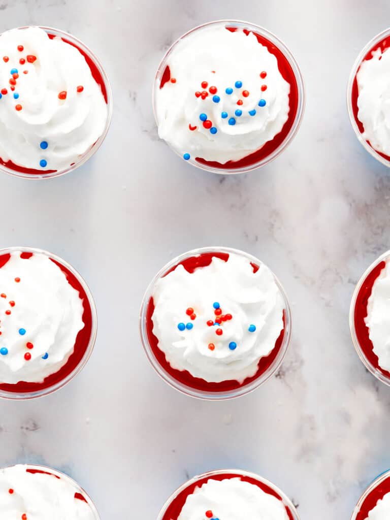 Top view of whipped cream topped patriotic jello cups. White marble surface.