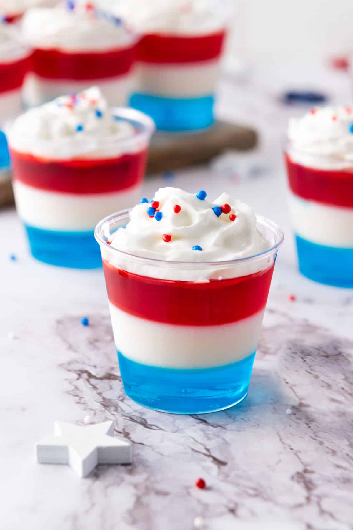Close up red, white and blue jello cups on a marbled surface.