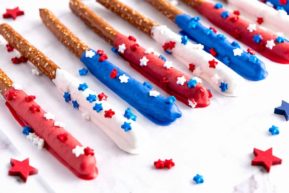 Several patriotic chocolate-covered pretzel rods with sprinkles on a flat white surface.
