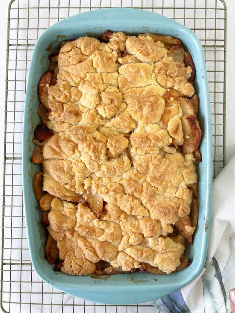 Blue rectangular dish with fresh apple cobbler with cake mix on a wire rack.