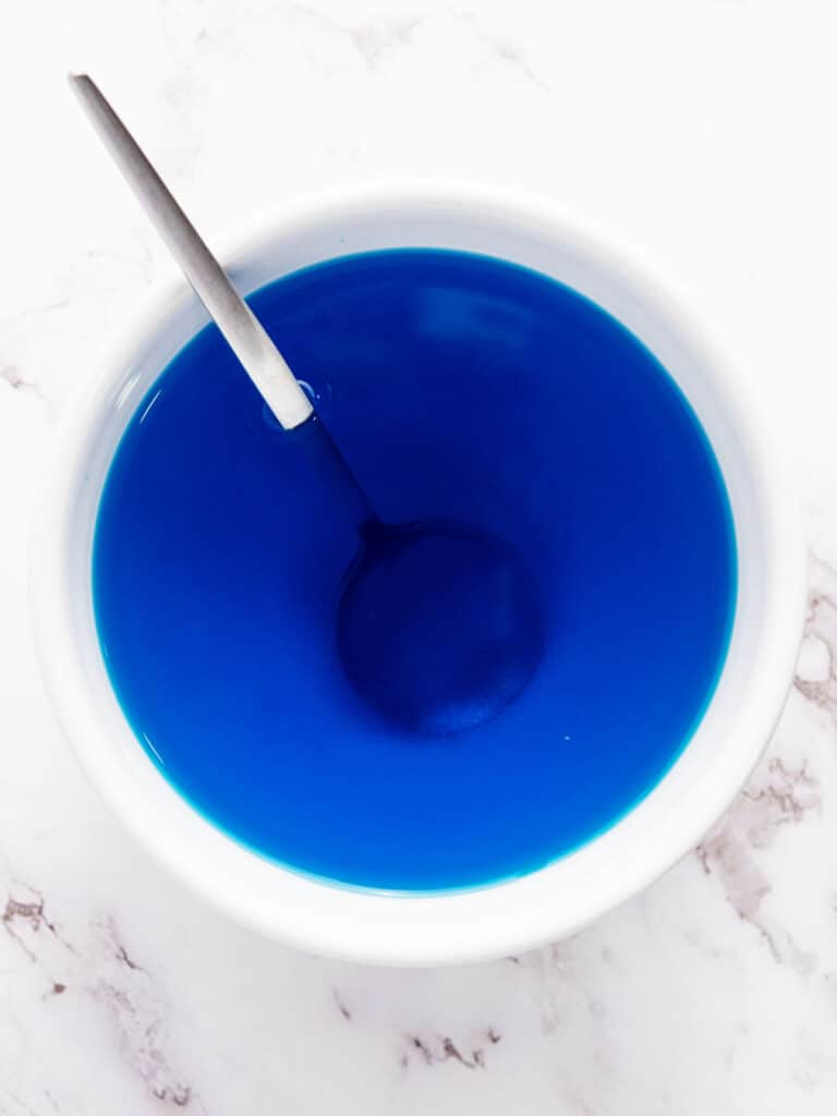 White bowl of blue jello. Marbled background.