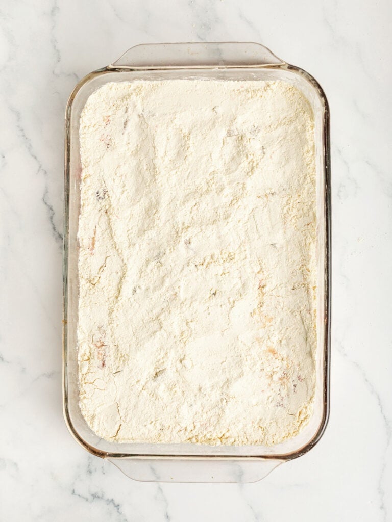 Evened-out cake mix layer on a glass baking dish. White marble surface. Top view.