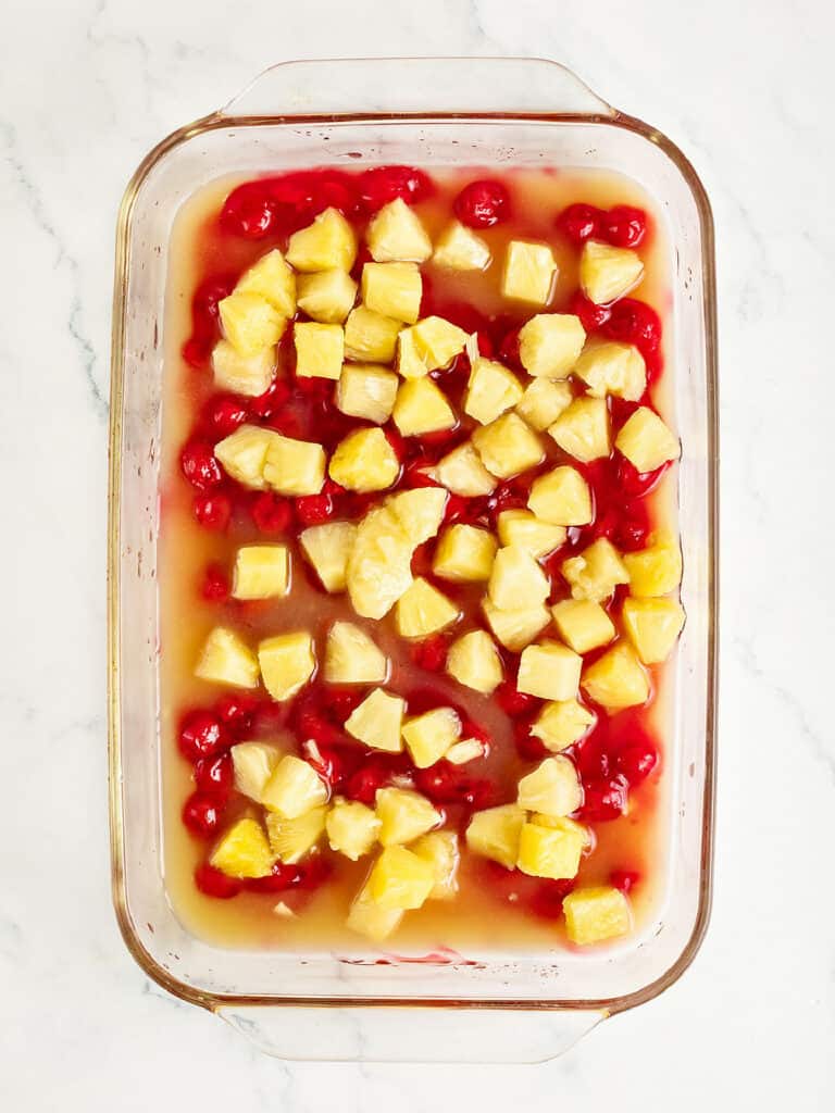 Chunks of pineapple and cherry pie filling in a glass rectangular dish. White marble surface.