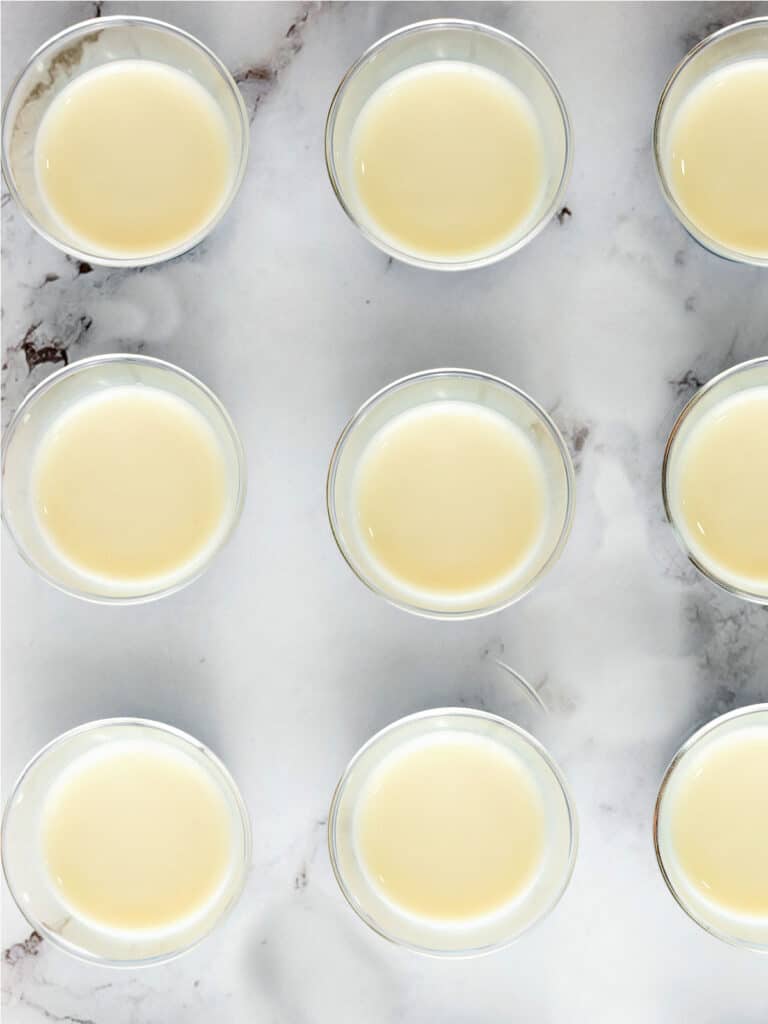 Condensed milk layer in rows of small plastic cups. Marble background.