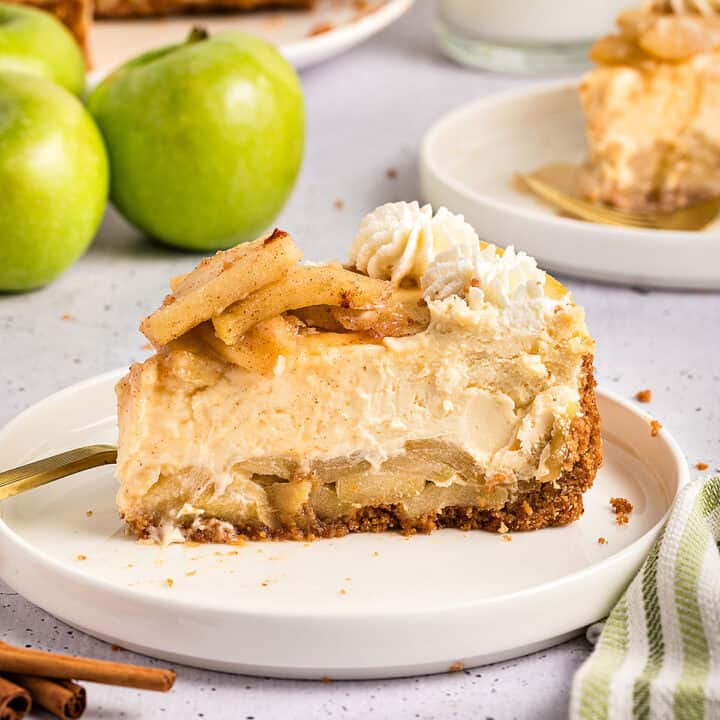 Single slice of apple cheesecake on a white plate. Light gray background, whole green apples.