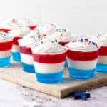 Red, white, blue jello cups with cream. Wooden board. White background.