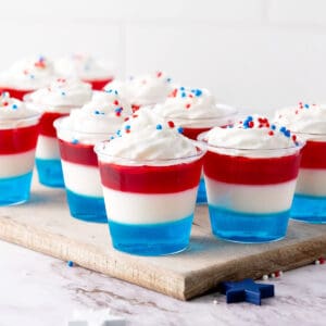 Red, white, blue jello cups with cream. Wooden board. White background.