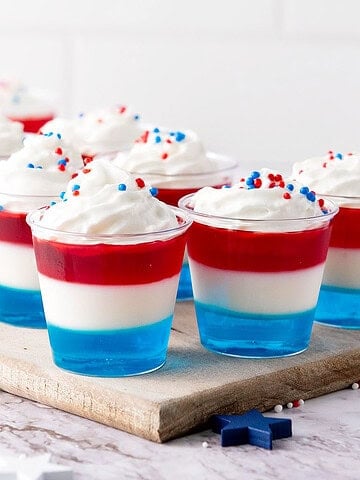 Red, white, blue jello cups with cream. Wooden board. White background.