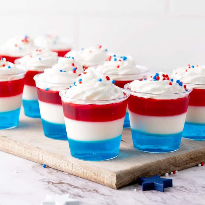 Red, white, blue jello cups with cream. Wooden board. White background.