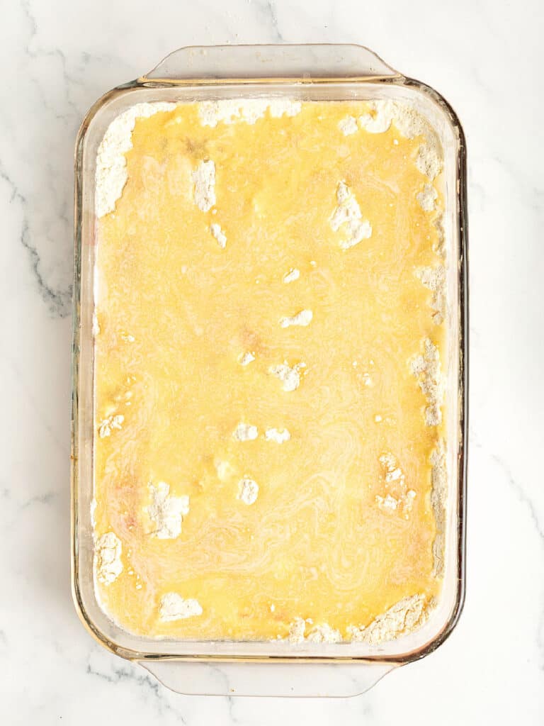Melted butter drizzled over yellow cake mix in a rectangular glass dish. White marble surface.